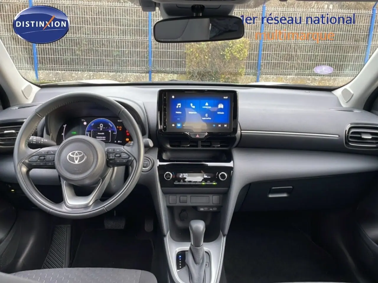 Vue intérieure frontale du tableau de bord et volant du Toyota Yaris Cross blanc, avec écran tactile central allumé.