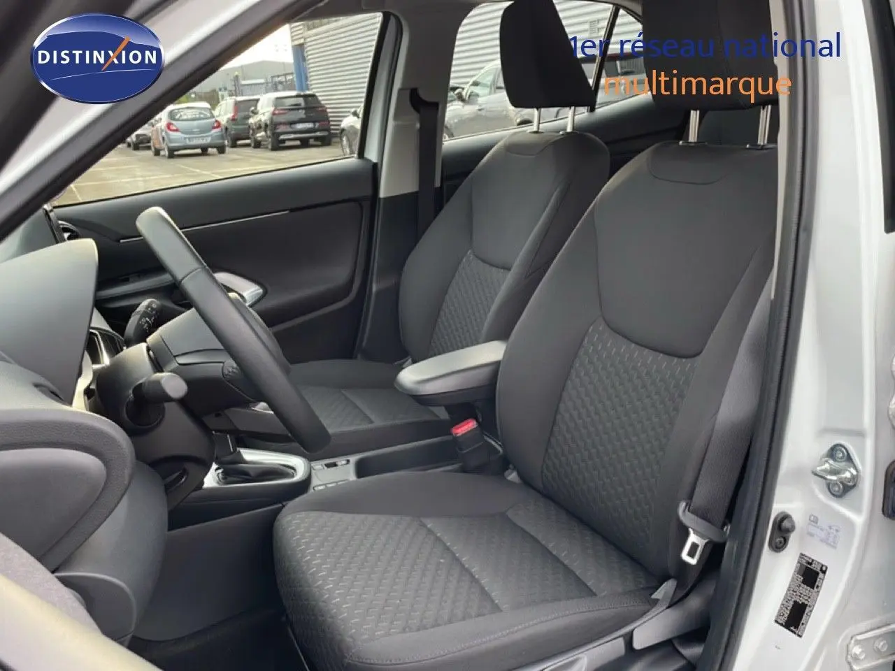 Vue intérieure côté conducteur de la Toyota Yaris Cross blanc pur 2024, montrant les sièges avant en tissu gris foncé.