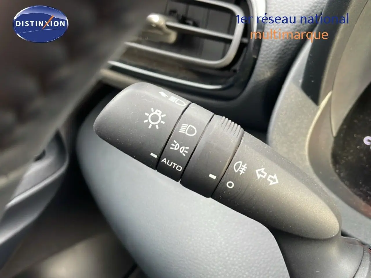 Gros plan sur la commande des phares et clignotants à gauche du volant dans l’habitacle d’une Toyota Yaris Cross blanche.