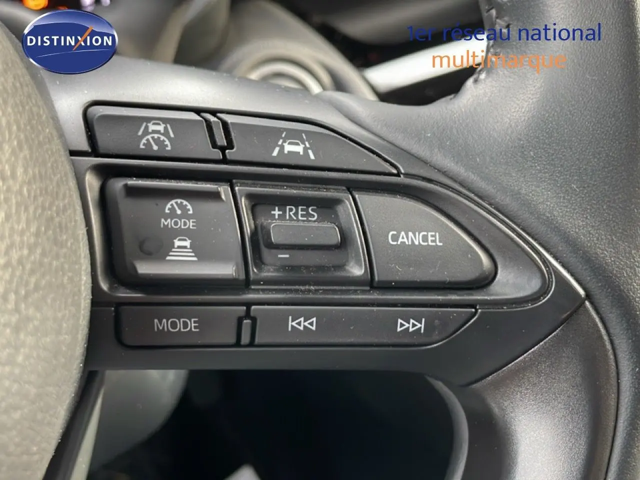 Gros plan sur les commandes au volant noir de la Toyota Yaris Cross 2024, boutons de régulateur de vitesse et multimédia visibles.