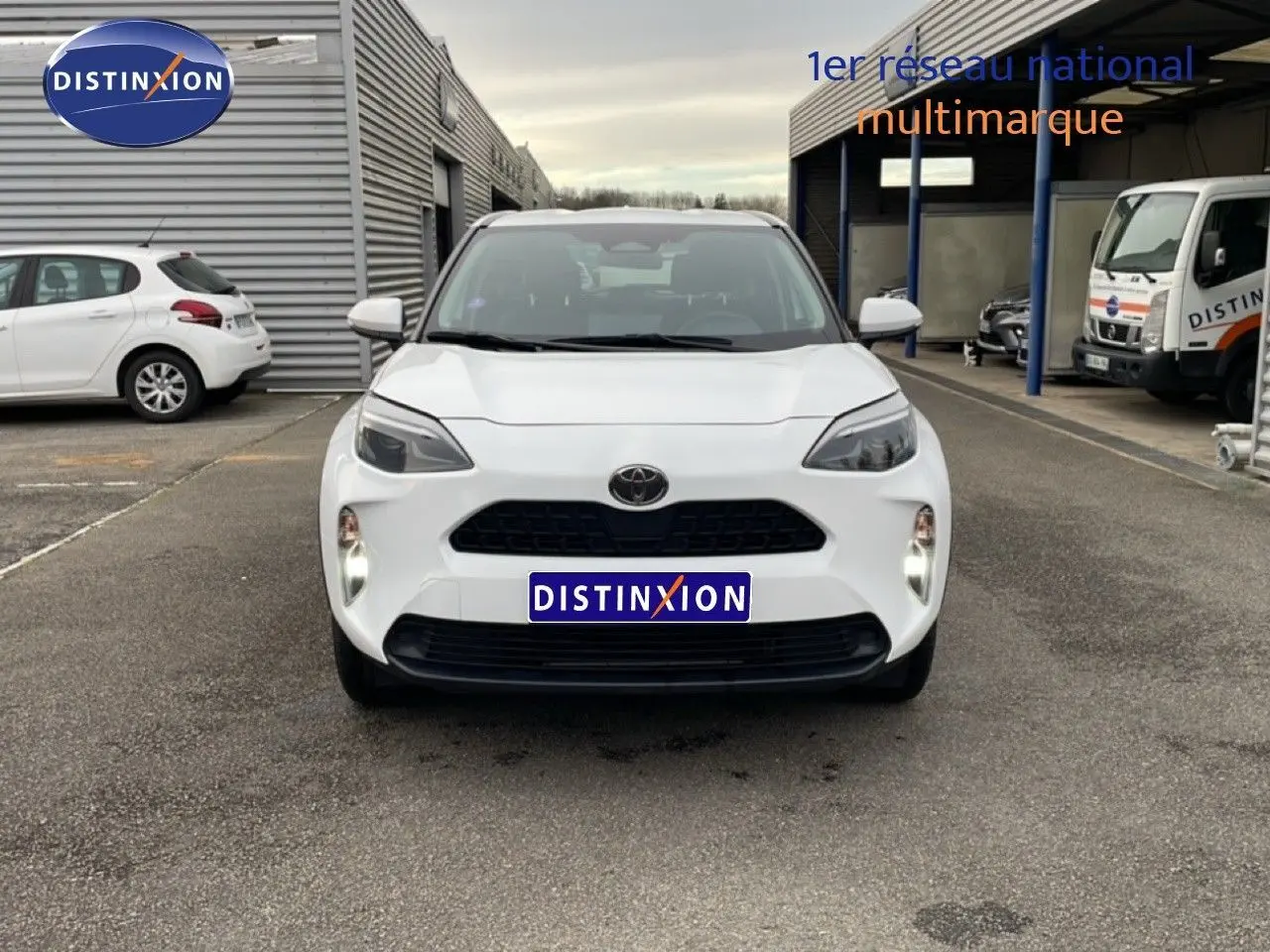 Vue de face d'une Toyota Yaris Cross 1.5 Hybrid blanche, avec calandre noire et phares LED allumés.