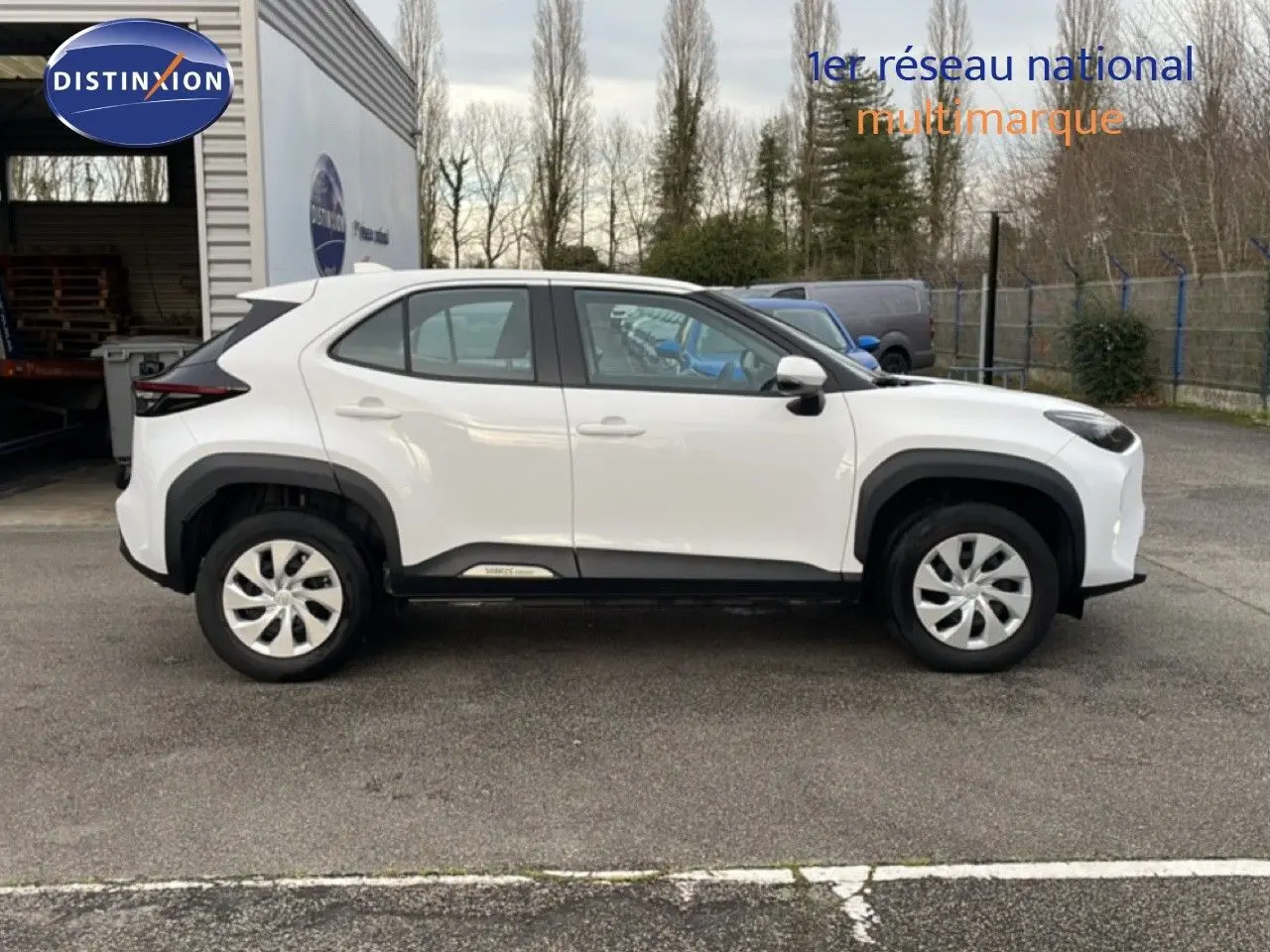 Vue de profil côté gauche d'une Toyota Yaris Cross 2024 blanche, soulignant ses lignes compactes et ses protections noires.