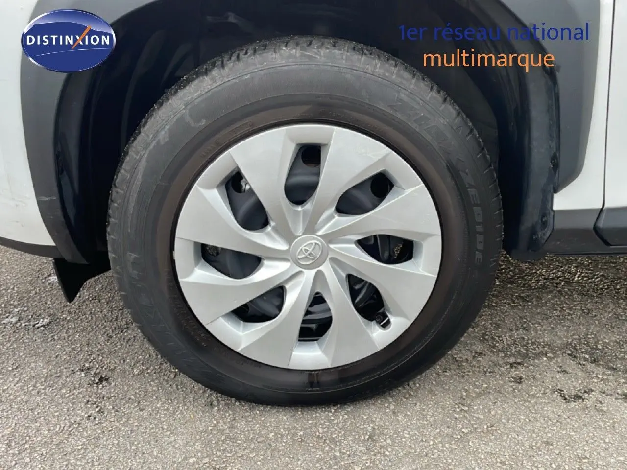 Gros plan sur la roue avant droite d'une Toyota Yaris Cross blanc pur, mettant en valeur la jante avec enjoliveur gris clair.