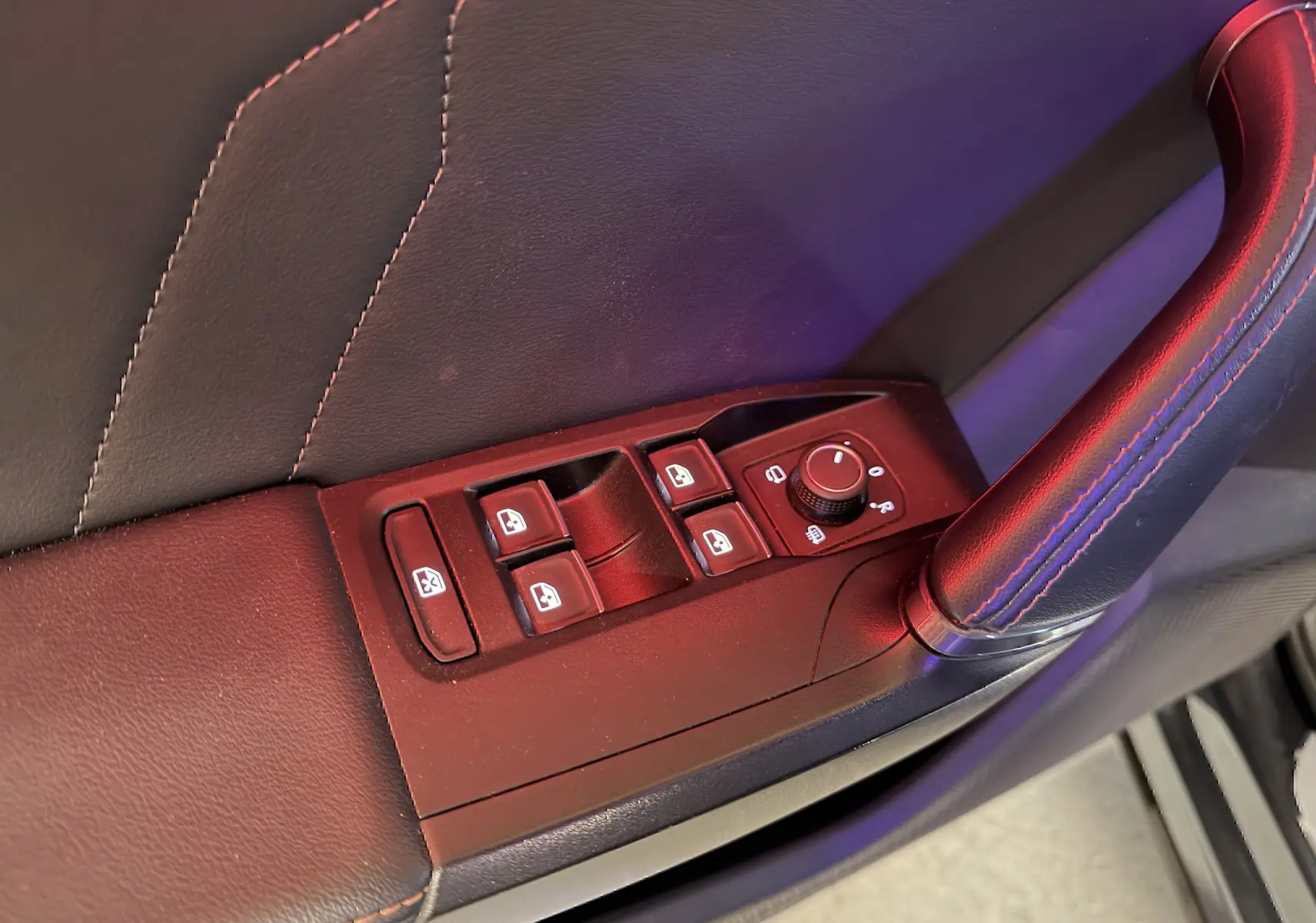 Gros plan sur les commandes des vitres et rétroviseurs côté conducteur du CUPRA Formentor gris clair, avec surpiqûres rouges sur la poignée.