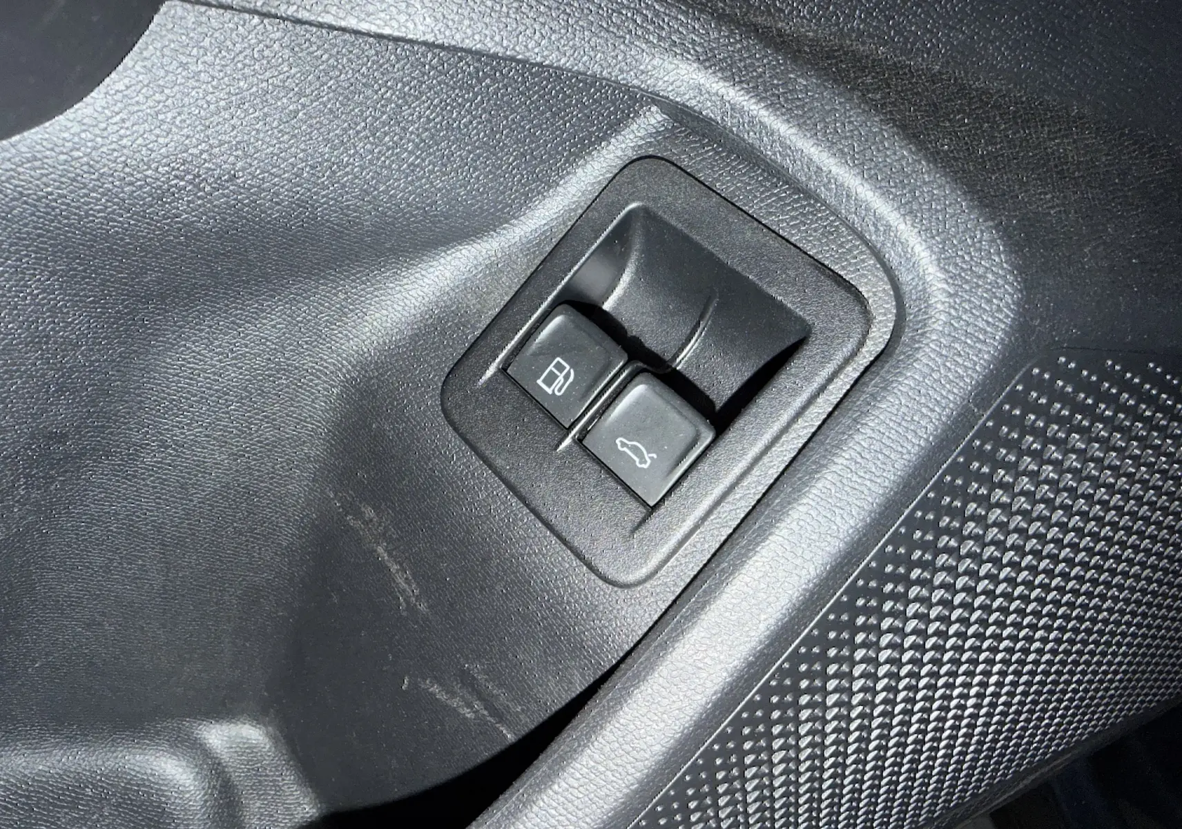 Gros plan sur les boutons d’ouverture de la trappe à carburant et du coffre, intérieur noir d’une CUPRA Formentor gris clair.