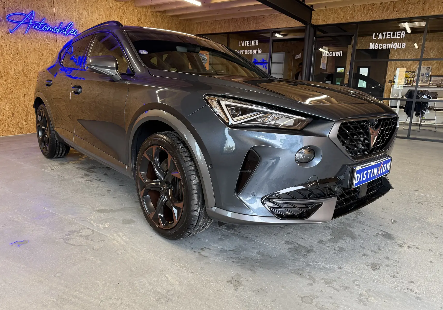 Vue 3/4 avant d'une CUPRA Formentor gris clair avec jantes cuivrées, garée en intérieur sur sol béton.