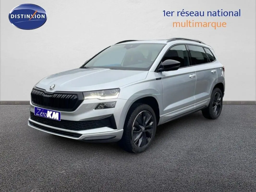 Vue 3/4 avant droite d’un Skoda Karoq argent 2025 avec barres de toit et jantes noires distinctives.