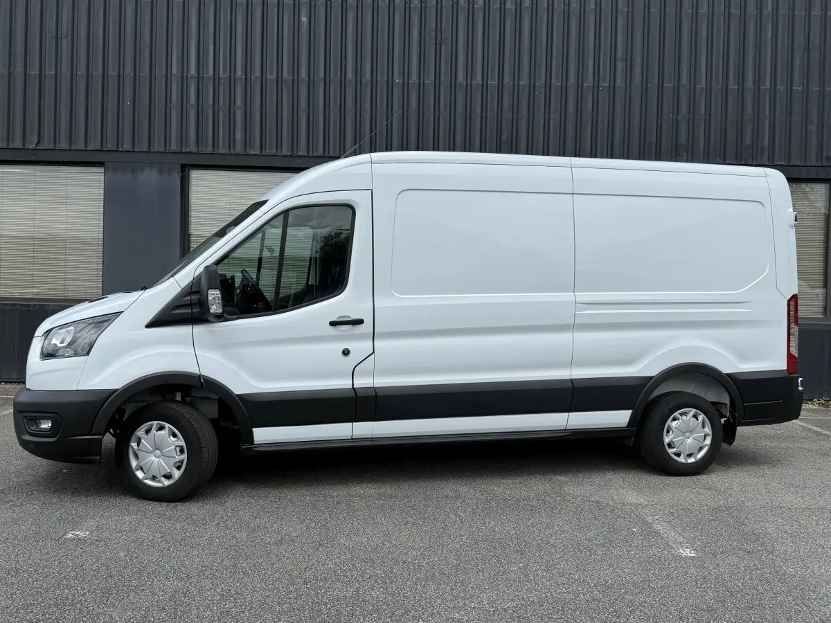 Vue de profil côté gauche d’un fourgon Ford Transit blanc avec bande noire basse et jantes tôles.