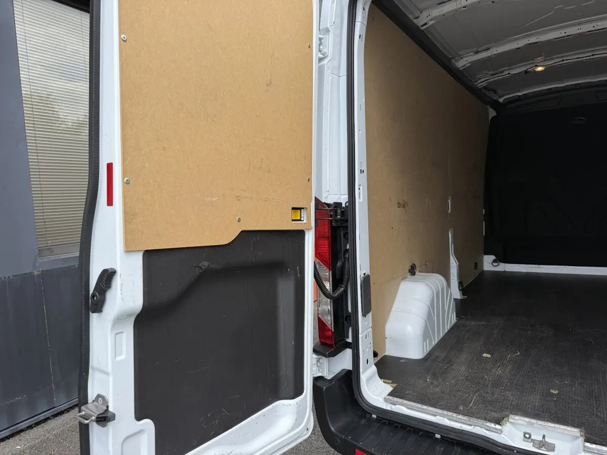 Vue arrière ouverte du fourgon Ford Transit blanc, montrant l'intérieur vide avec parois en bois et plancher noir antidérapant.
