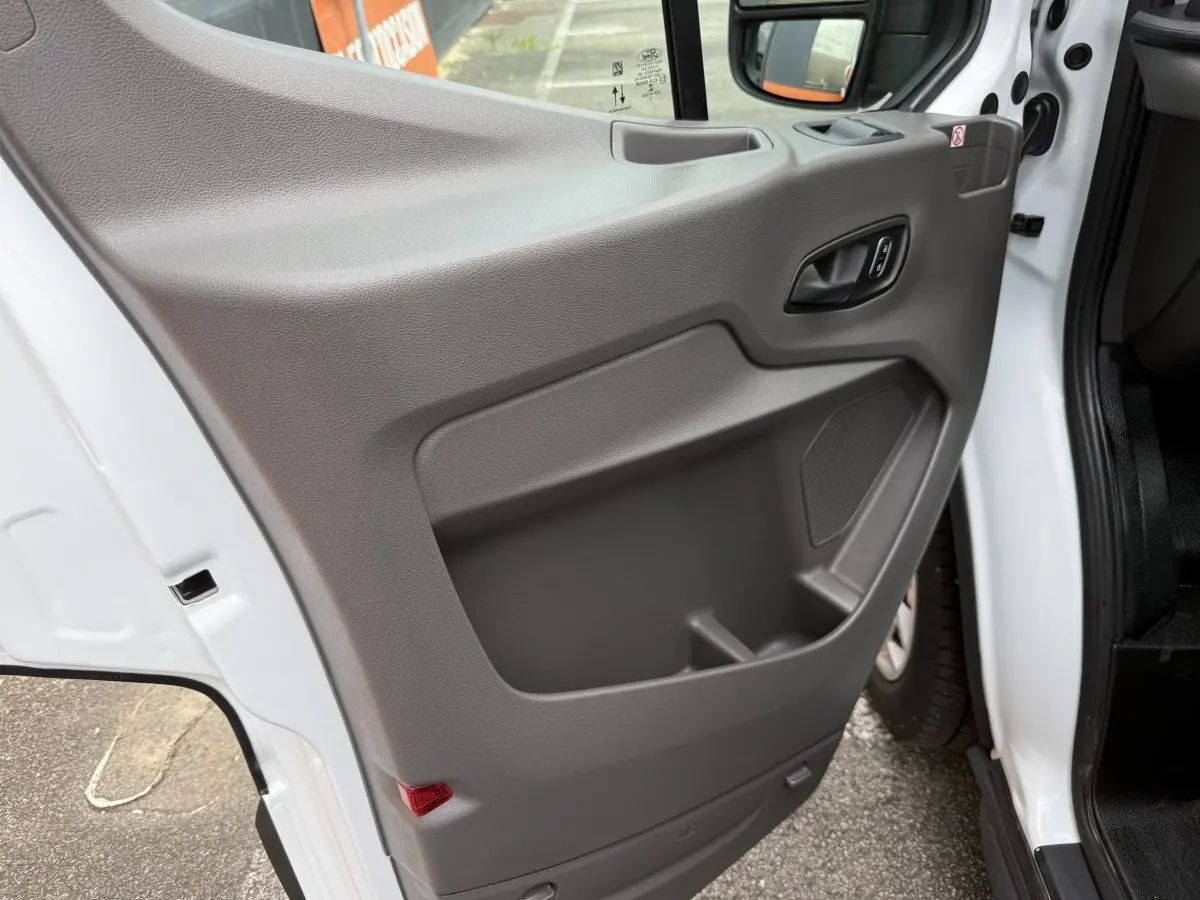 Vue rapprochée de la porte avant gauche grise du Ford Transit Fourgon blanc, montrant la poignée et le rangement intégré.