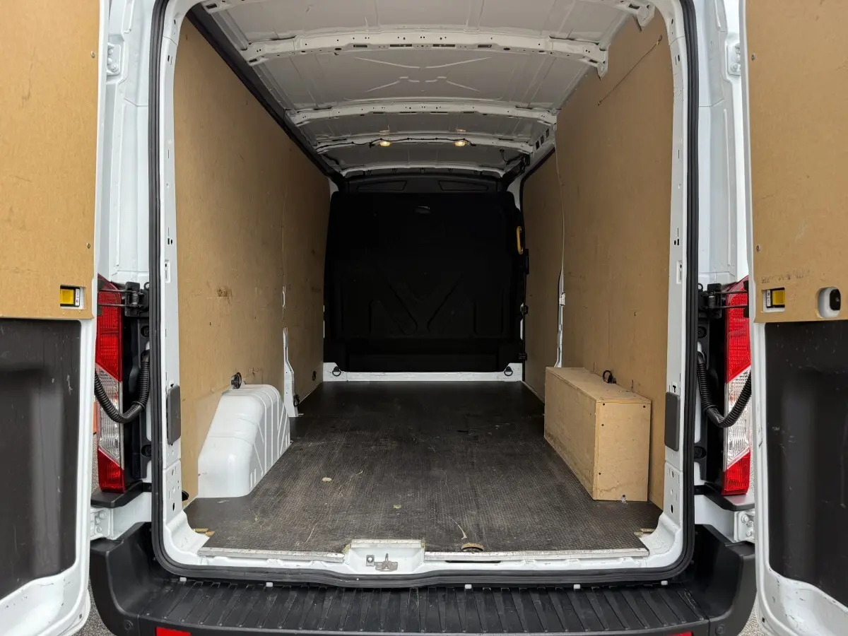 Vue arrière du fourgon Ford Transit blanc 2024 avec portes ouvertes, montrant l'espace de chargement vide et cloison pleine.