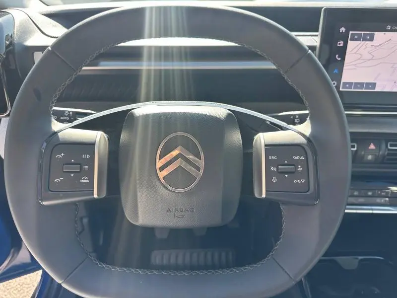 Vue rapprochée du volant noir de la Citroën C3 2025 avec commandes intégrées et écran tactile GPS en arrière-plan.