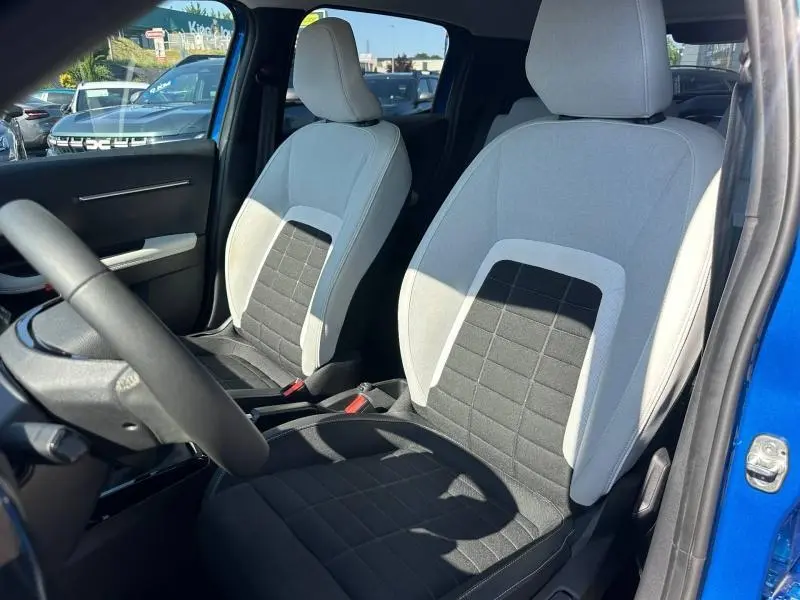 Vue intérieure côté conducteur de la Citroën C3 2025 avec sièges tissu clair et noir, porte ouverte sur carrosserie Bright Blue.