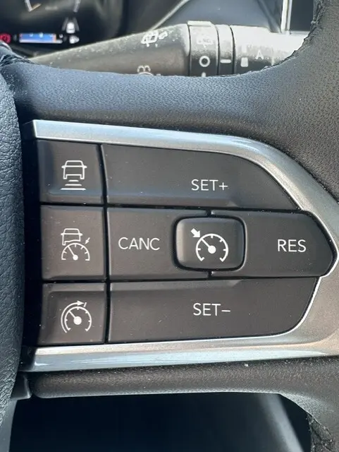 Gros plan sur les commandes du régulateur de vitesse au volant du Jeep Compass noir 2025, boutons noirs avec marquages blancs.