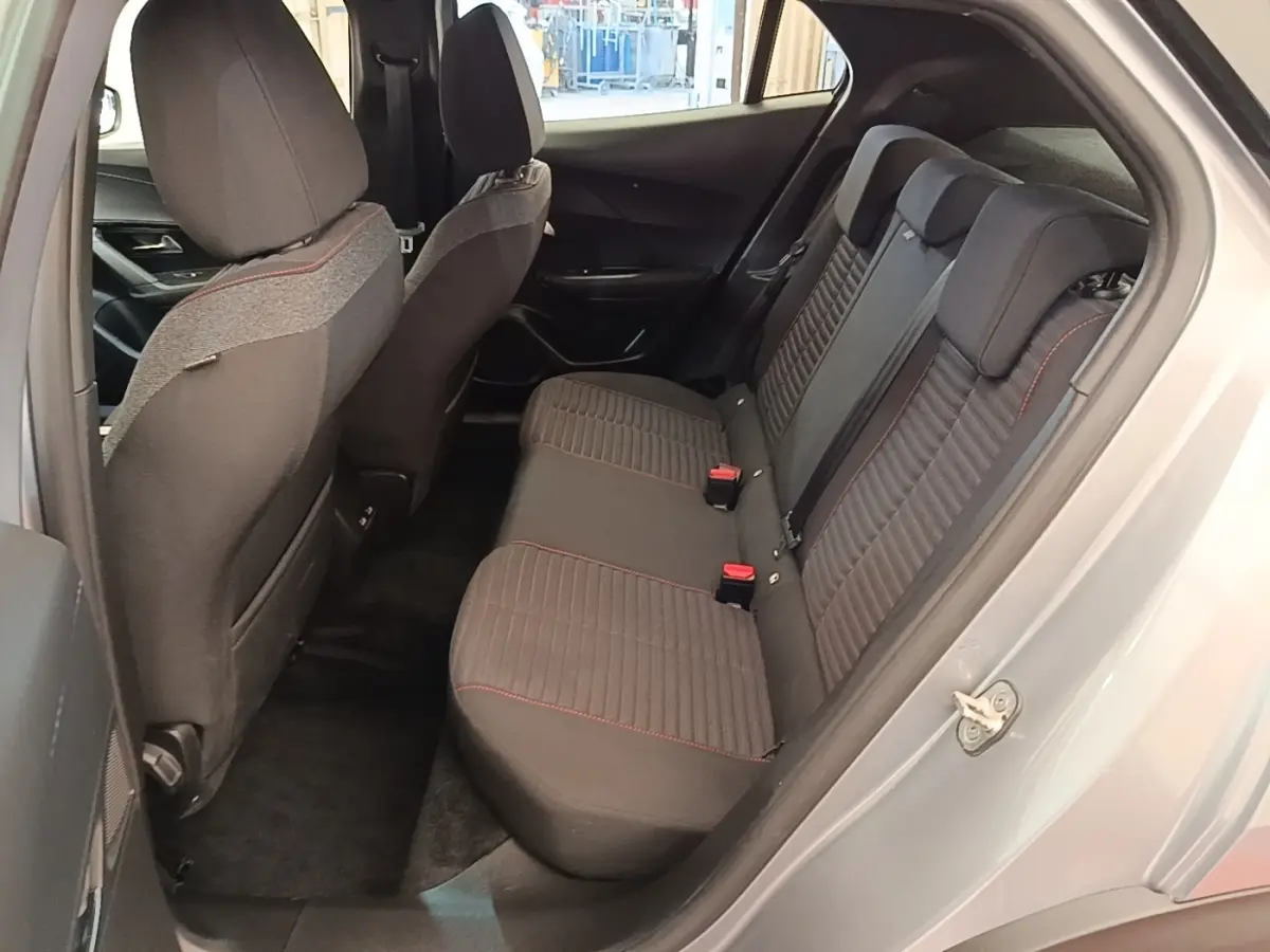 Vue côté gauche de l’habitacle arrière gris clair du Peugeot E-2008 électrique avec sièges tissu noir et surpiqûres rouges.