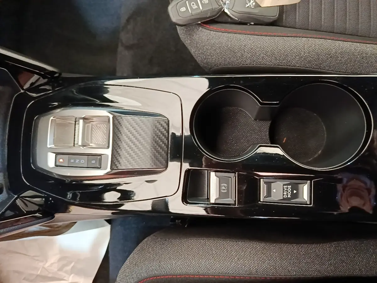 Vue plongeante sur la console centrale noire brillante du Peugeot E-2008 électrique avec sélecteur de vitesse et porte-gobelets.