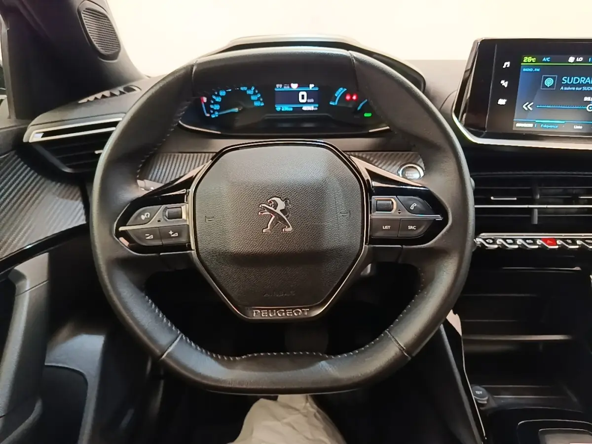 Vue intérieure centrée sur le volant cuir noir du Peugeot E-2008 électrique avec tableau de bord digital et écran tactile.