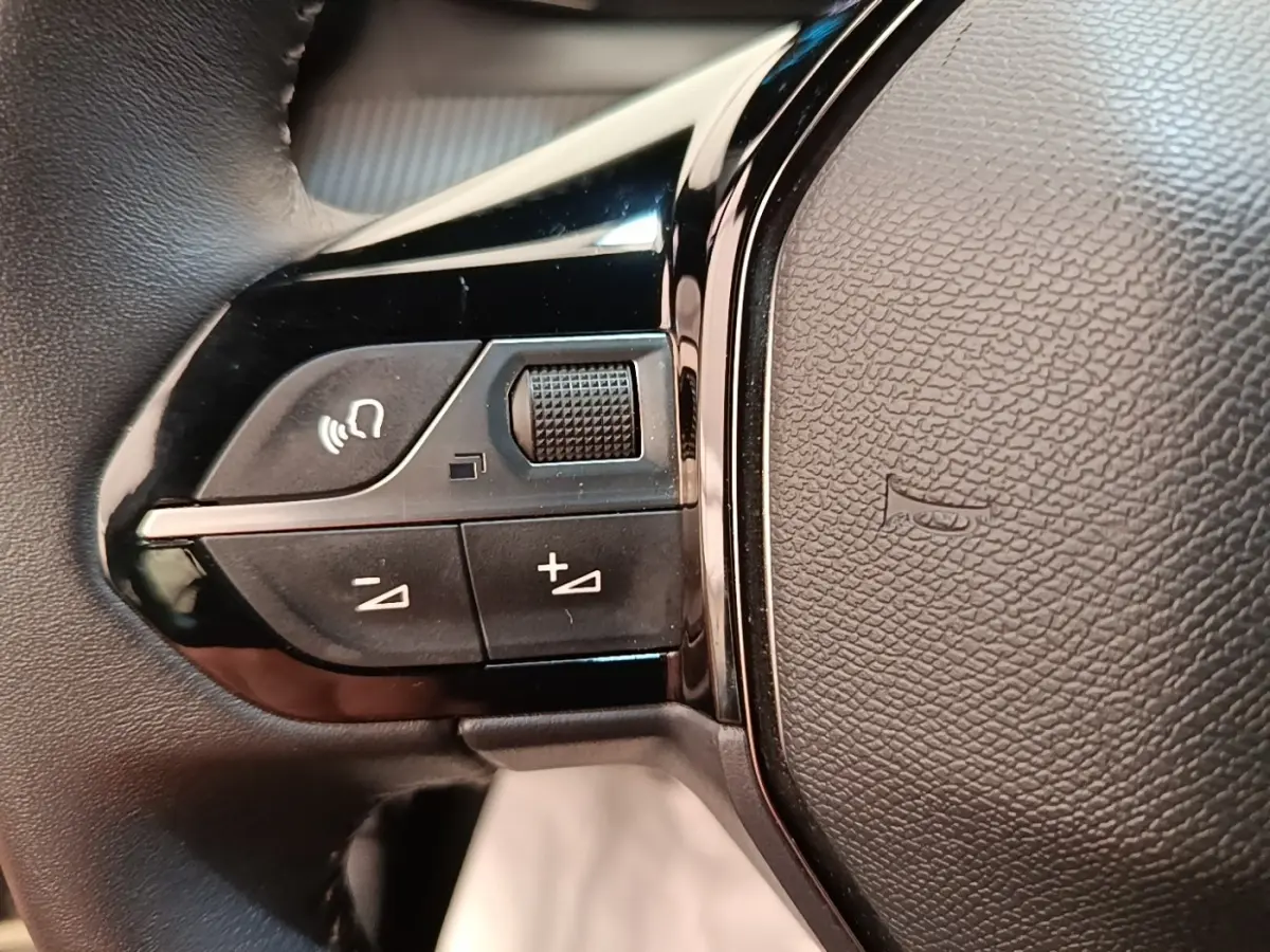 Gros plan sur les commandes gauche du volant cuir noir du Peugeot E-2008 électrique gris clair 2023.