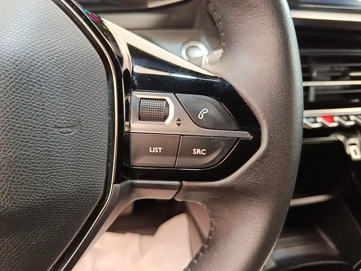 Gros plan sur la partie gauche du volant cuir noir du Peugeot E-2008 électrique, avec commandes intégrées.