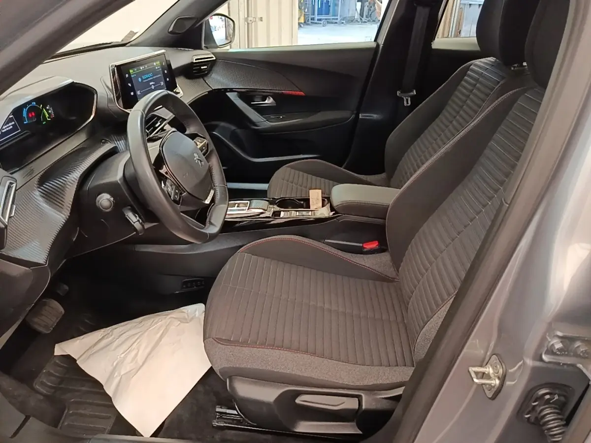 Vue intérieure côté conducteur du Peugeot E-2008 électrique gris clair 2023, avec tableau de bord digital et sièges tissu.