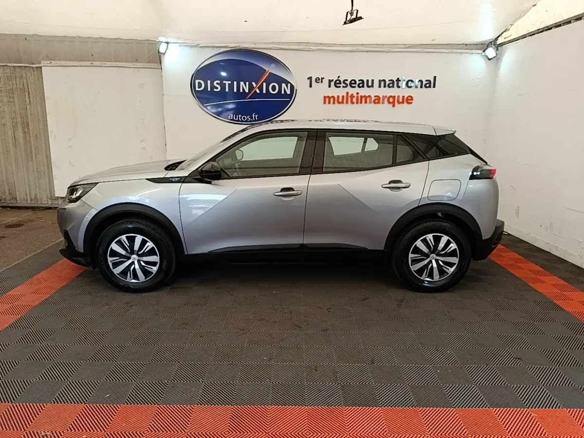 Profil côté gauche d’un Peugeot E-2008 électrique gris clair, avec jantes distinctives et toit noir en showroom.