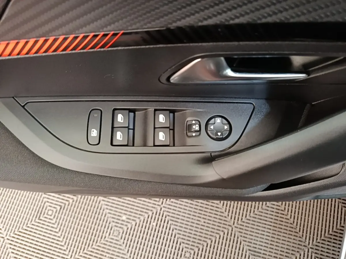 Gros plan sur la commande des vitres et rétroviseurs côté conducteur de la Peugeot E-2008 électrique gris clair, avec poignée de porte.