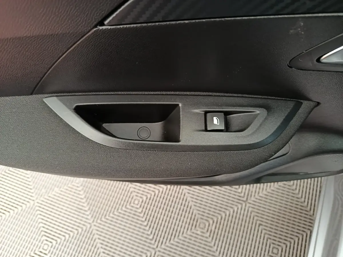 Gros plan sur la poignée intérieure et commande de lève-vitre côté droit d’un Peugeot E-2008 électrique gris clair.