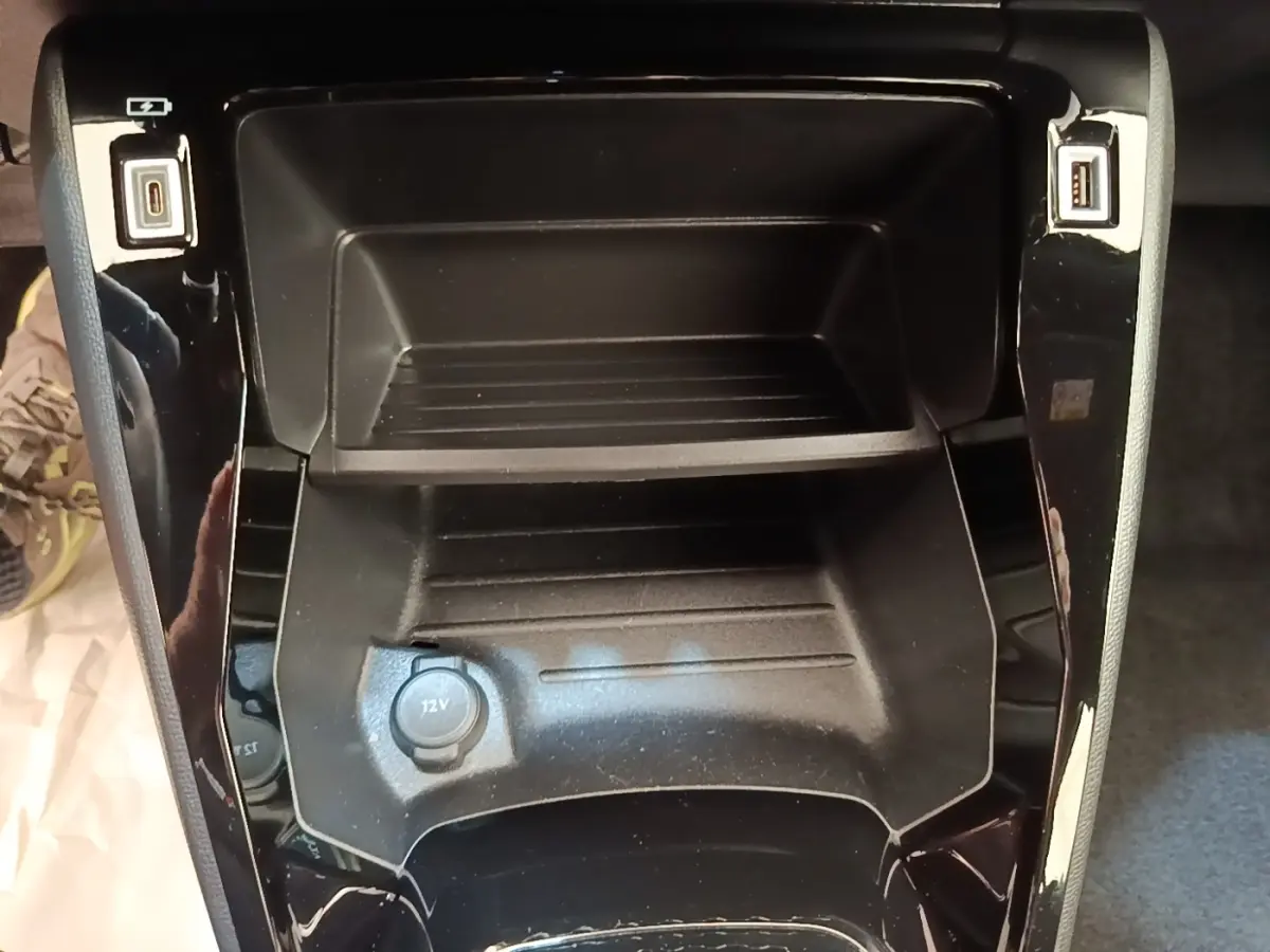 Vue rapprochée du rangement central noir avec prise 12V et ports USB du Peugeot E-2008 électrique gris clair.