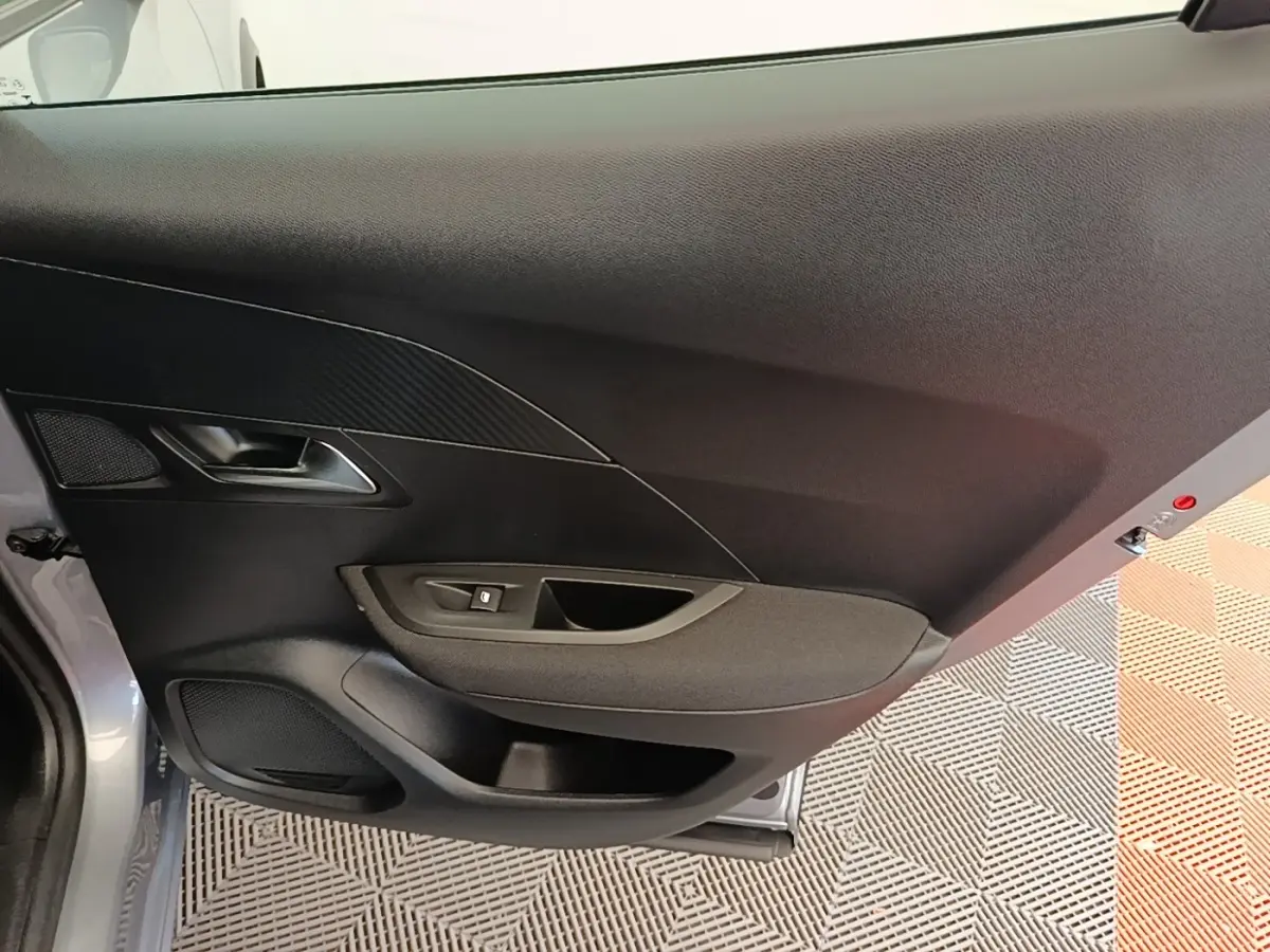 Vue rapprochée de la porte avant gauche gris clair du Peugeot E-2008 électrique avec poignée et commande de vitre.