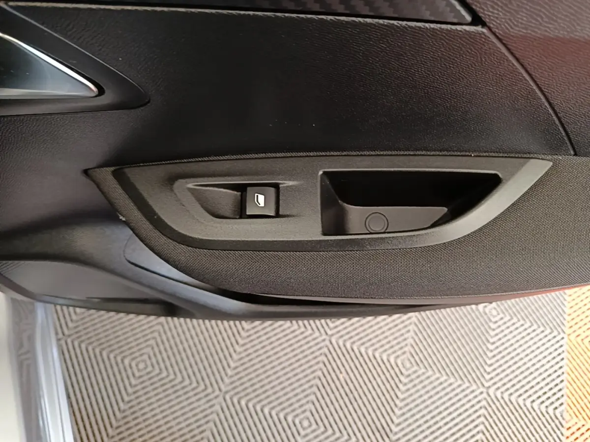 Gros plan sur la poignée intérieure et le bouton de lève-vitre côté conducteur du Peugeot E-2008 gris clair électrique.