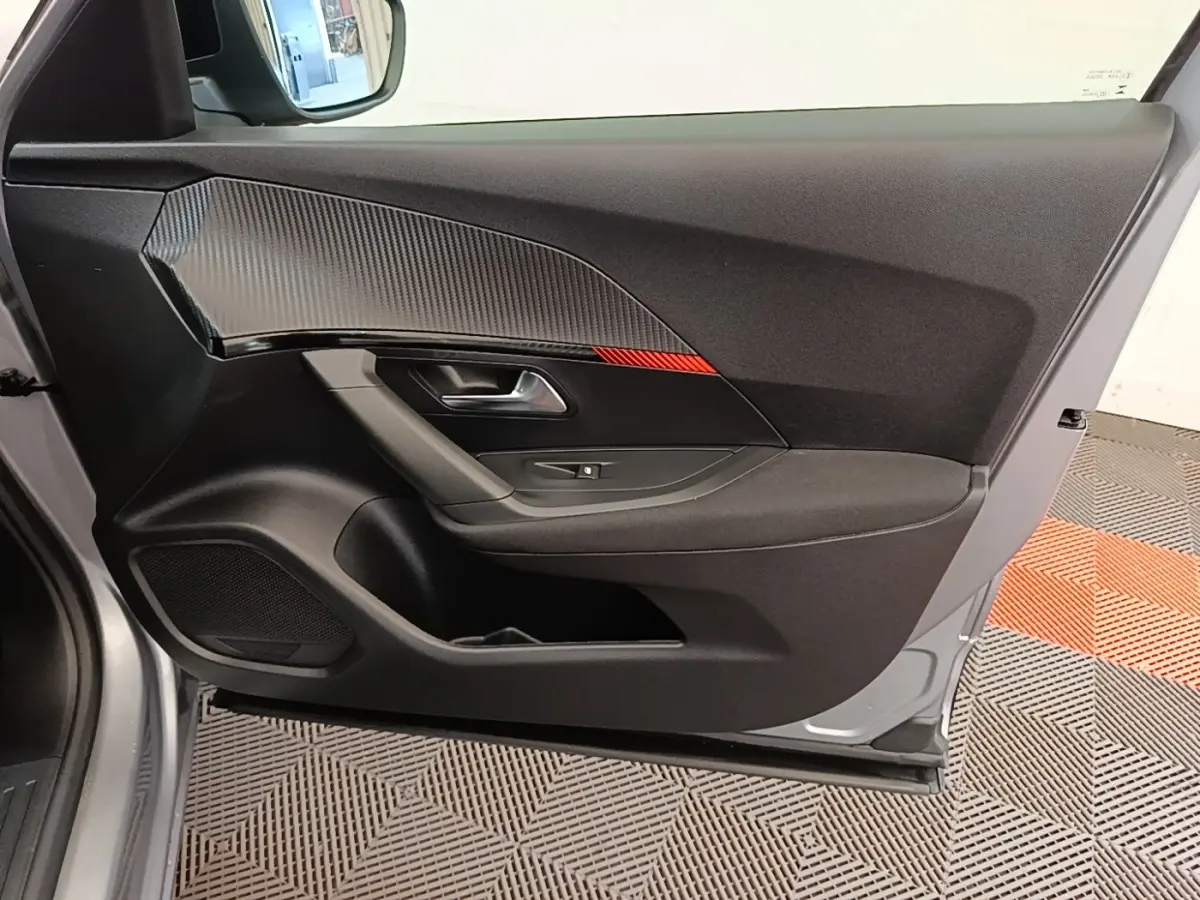Vue latérale gauche de la porte intérieure gris clair du Peugeot E-2008 électrique avec insert carbone et bande rouge décorative.