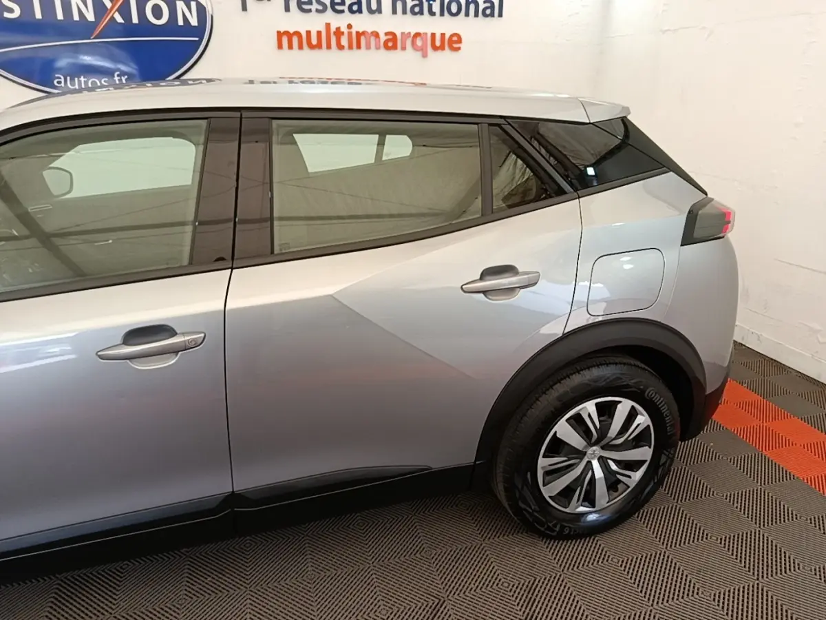 Vue latérale côté droit du Peugeot E-2008 électrique gris clair, mettant en valeur la porte arrière et la roue arrière.