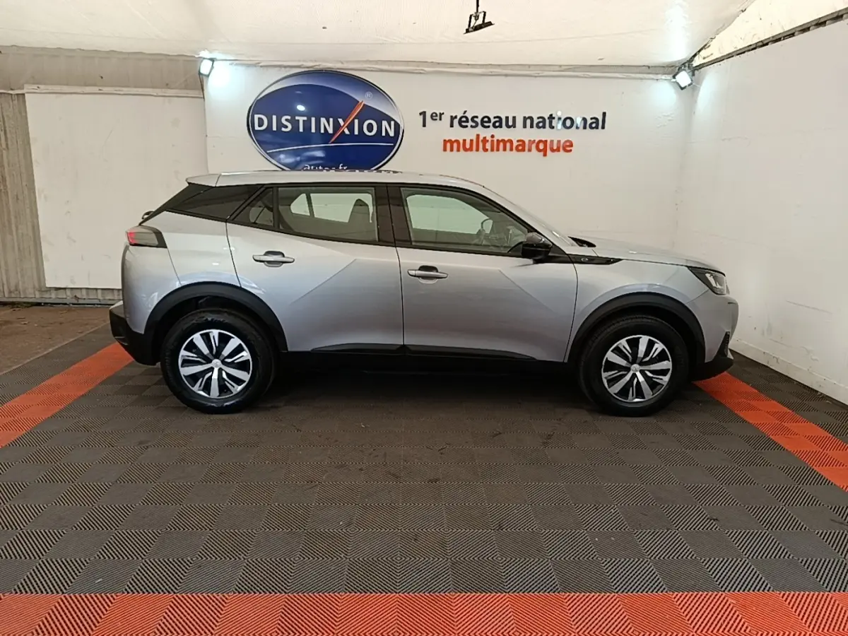 Profil droit d'un Peugeot E-2008 électrique gris clair 2023, avec toit noir et jantes distinctives en concession.