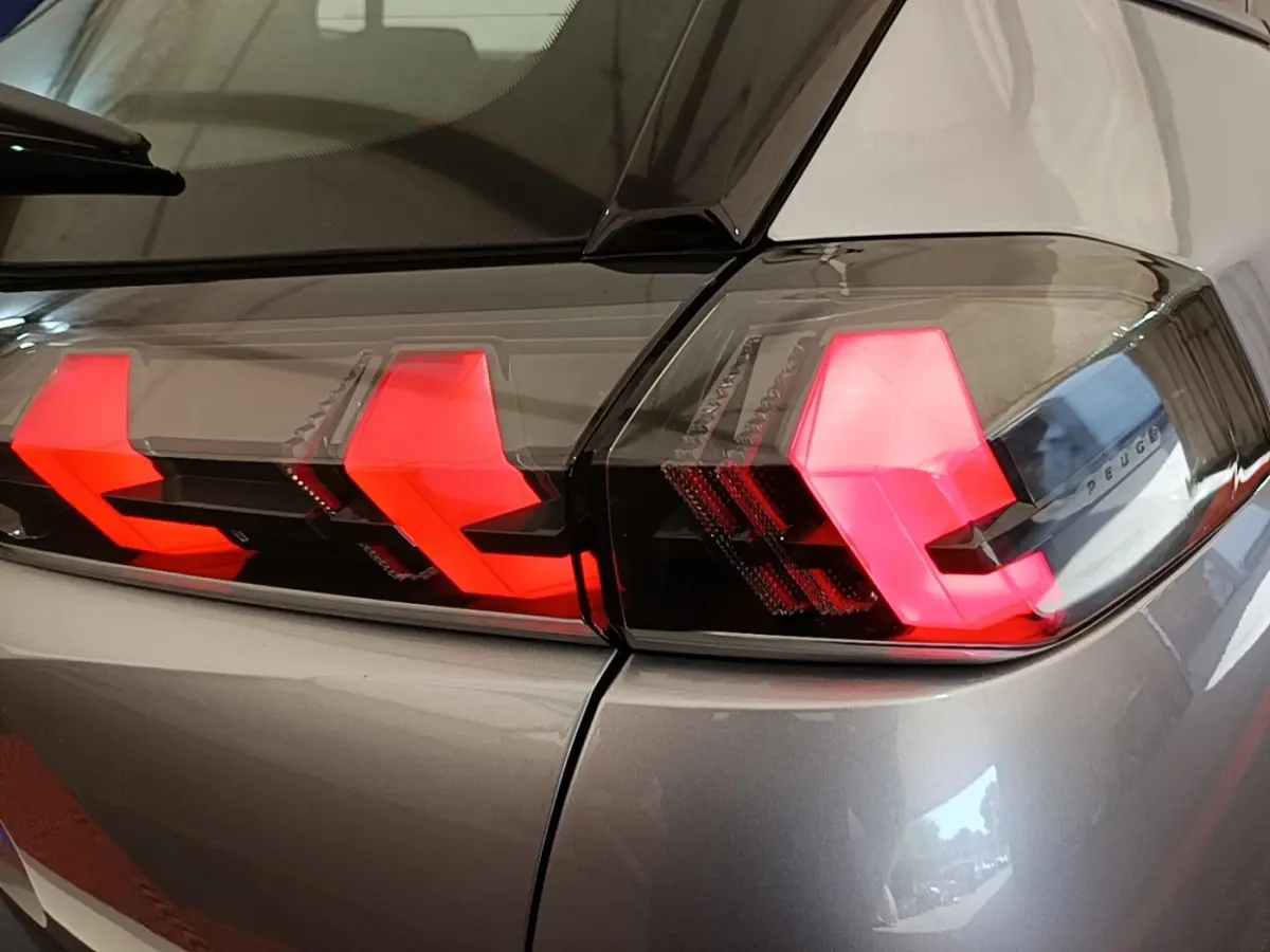 Gros plan sur les feux arrière allumés du Peugeot E-2008 électrique gris clair, vue côté droit arrière.