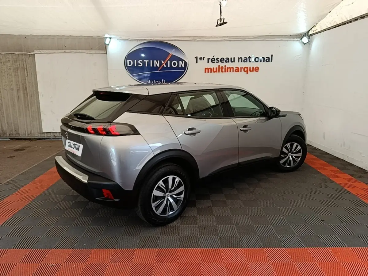 Vue 3/4 arrière droite d’un Peugeot E-2008 électrique gris clair avec toit noir dans un showroom.