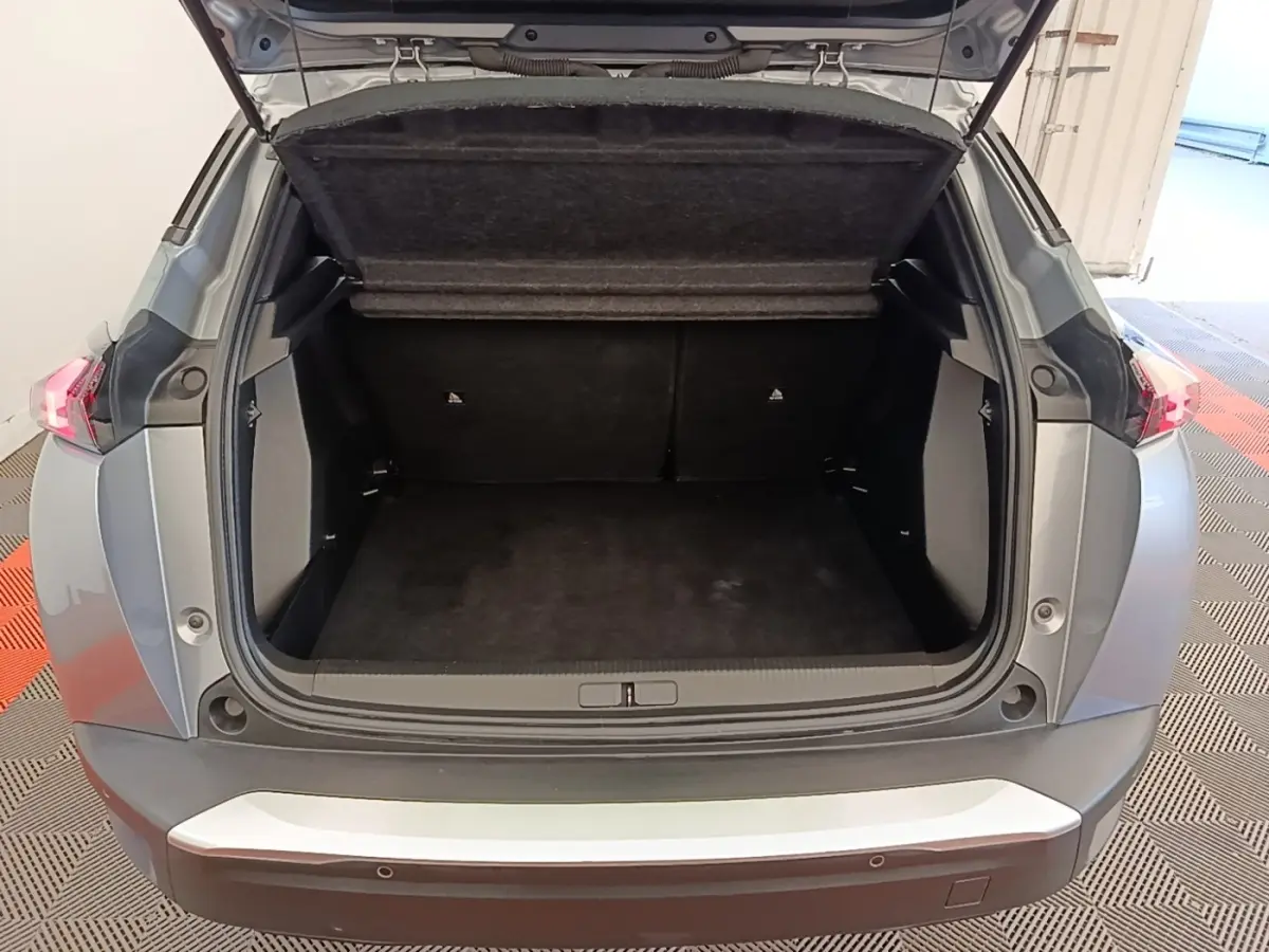 Coffre ouvert vu de l'arrière d'un Peugeot E-2008 électrique gris clair, montrant l'espace de chargement vide.