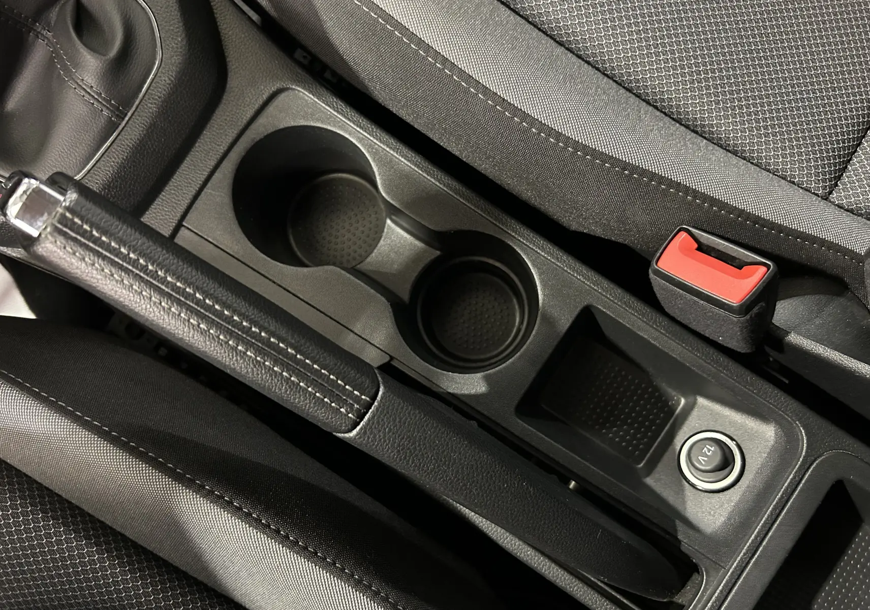 Gros plan sur la console centrale noire de la SEAT Ibiza 2019, avec frein à main, porte-gobelets et prise 12V visible.