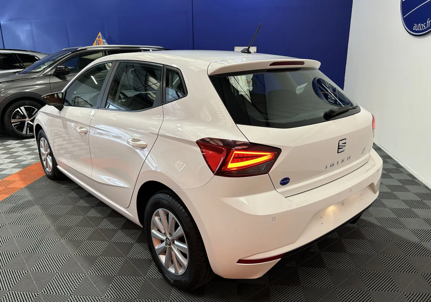 Vue 3/4 arrière droite d'une SEAT Ibiza blanche 2019 avec feux arrière LED allumés dans un showroom.