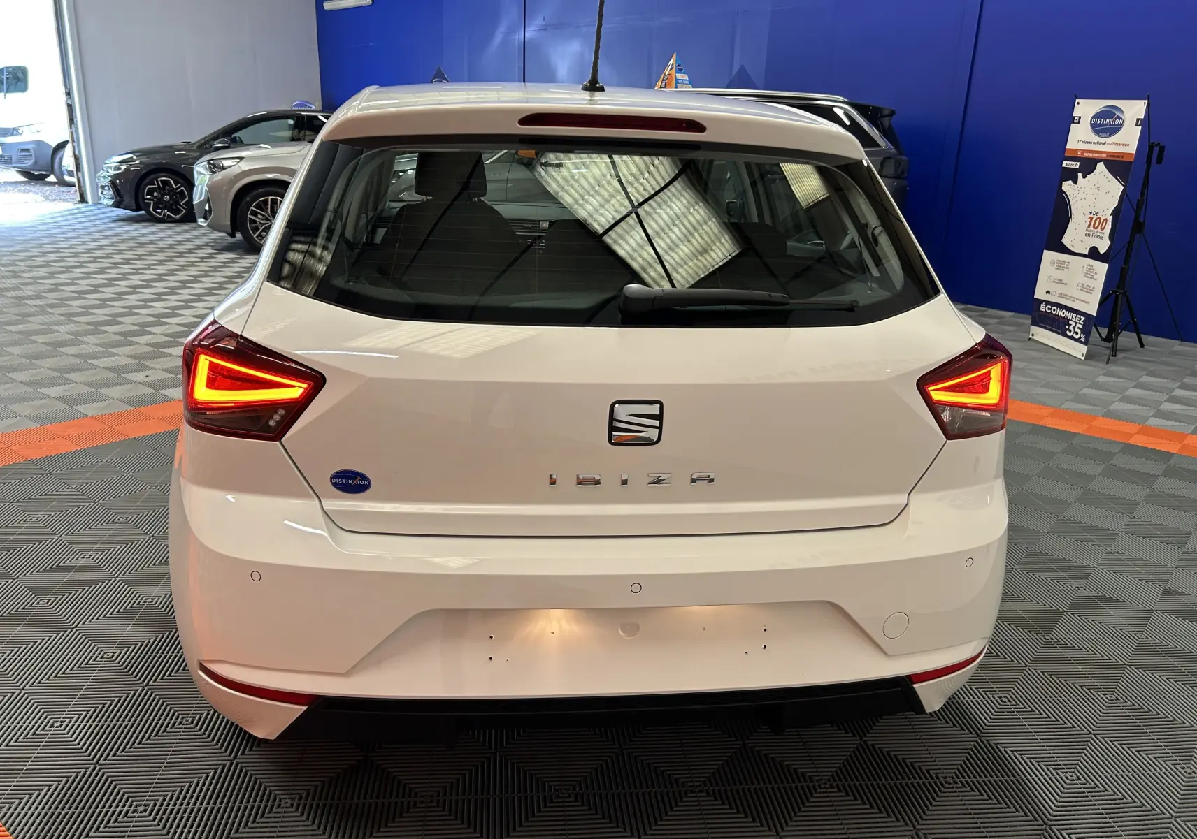 Vue arrière d'une SEAT Ibiza blanche de 2019 avec feux arrière allumés dans un showroom intérieur.