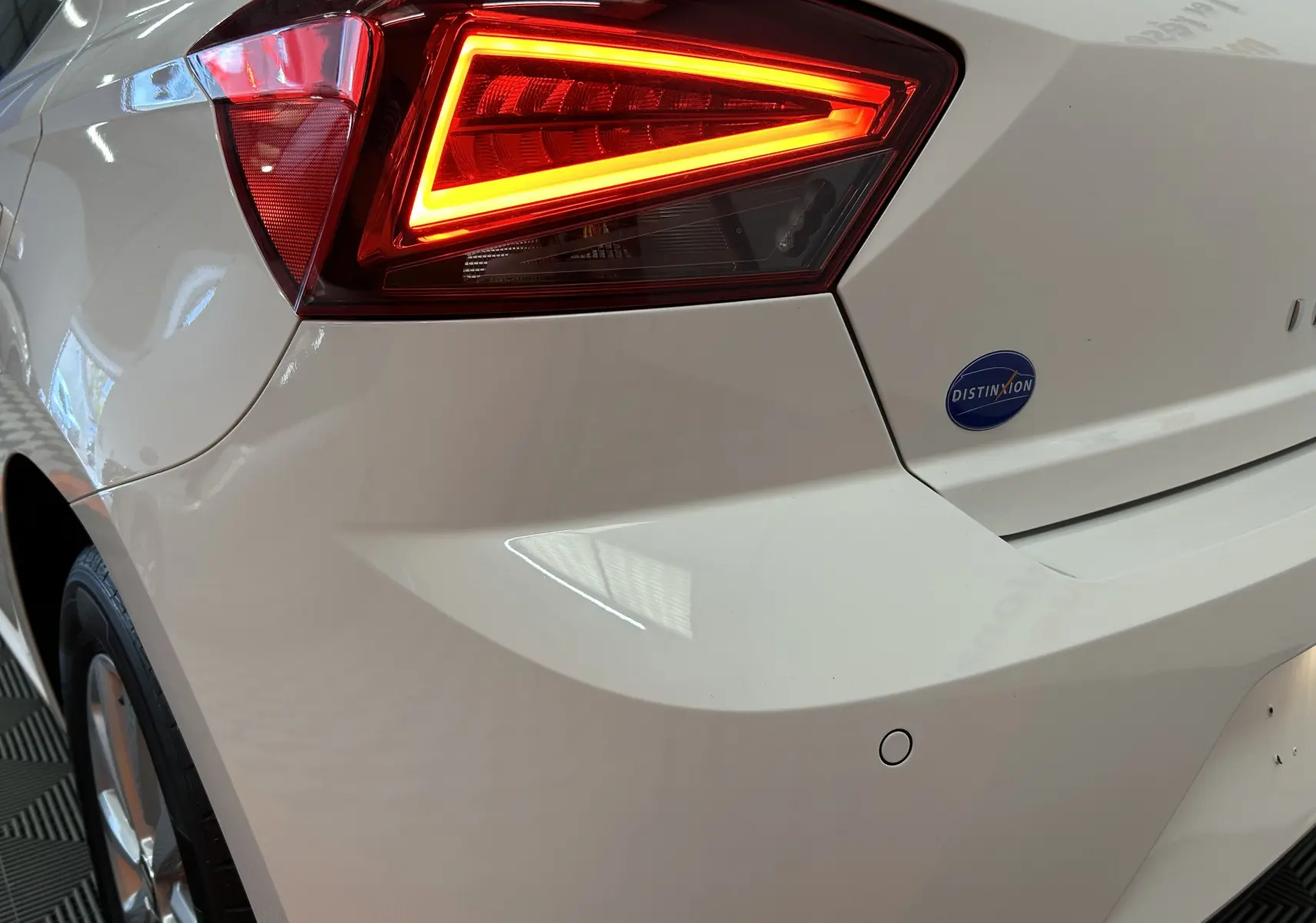 Gros plan sur le feu arrière droit allumé d'une SEAT Ibiza blanche de 2019 avec badge Distinxion sur le coffre.