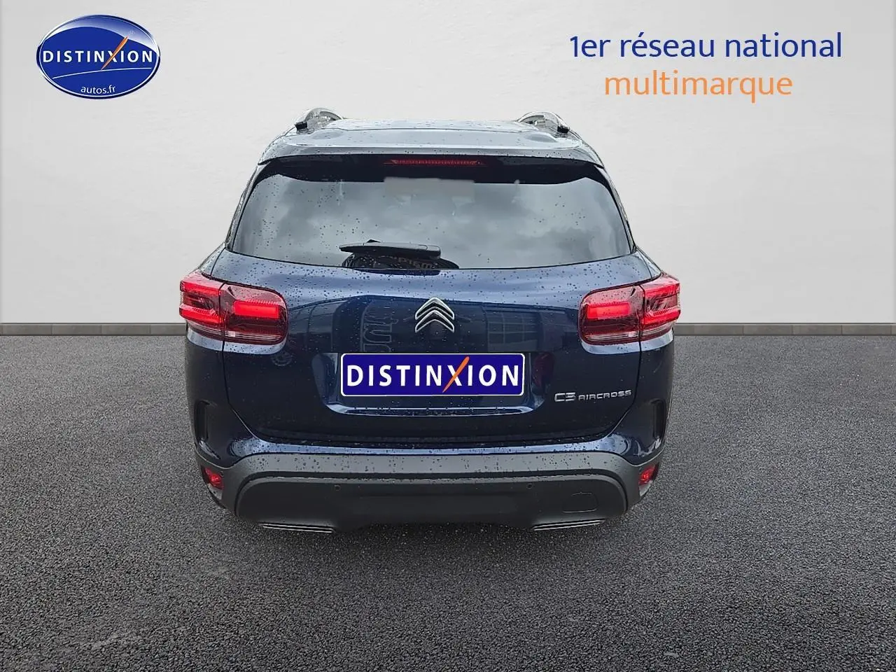 Vue arrière d'un Citroën C5 Aircross bleu eclipse avec toit noir et barres de toit, sous la pluie.