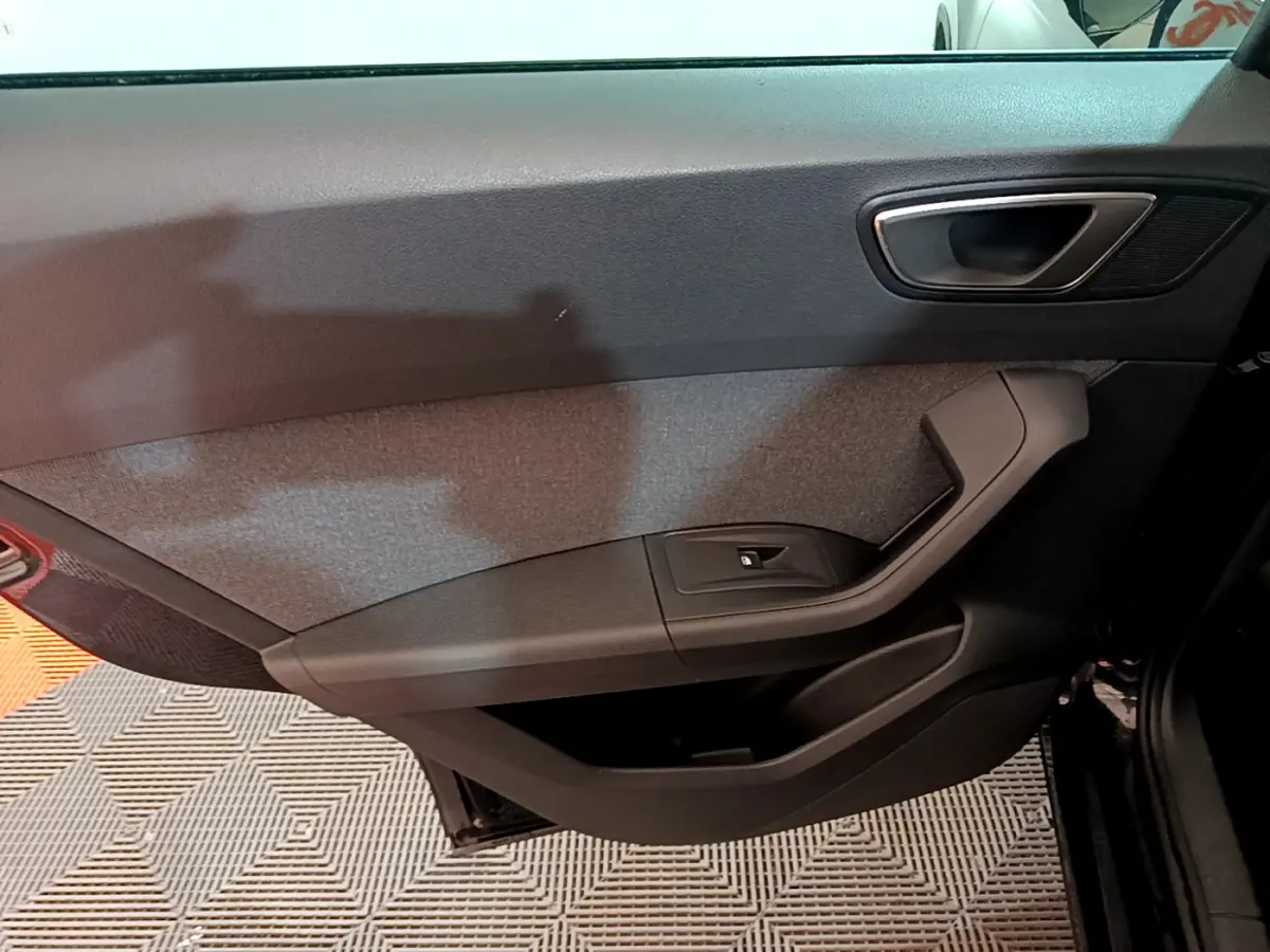 Intérieur côté gauche de la porte avant noire du SEAT Ateca 2022 avec poignée argentée et bouton de vitre électrique.
