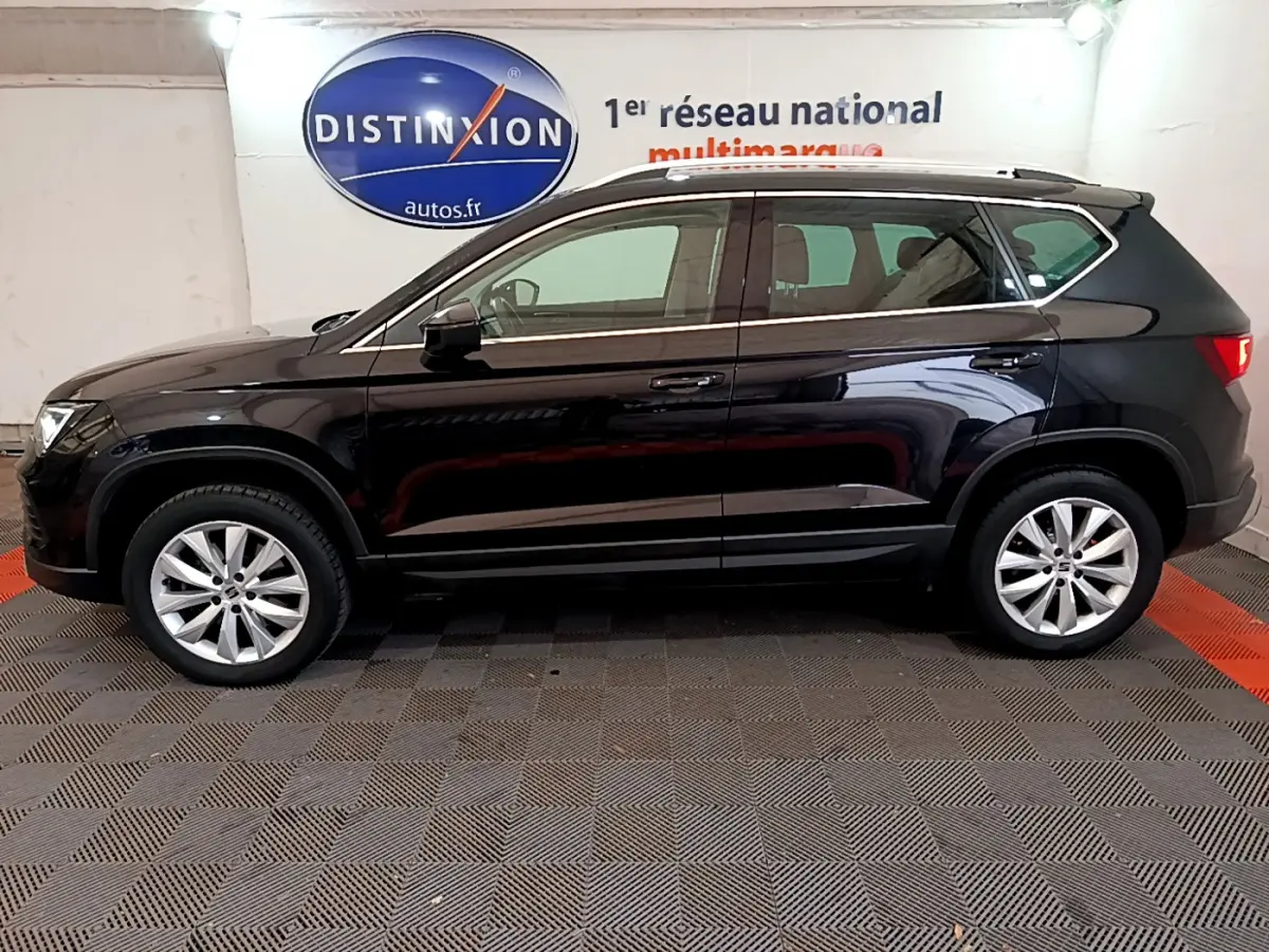 Profil côté gauche d'un SUV SEAT Ateca noir 2022 garé en intérieur avec jantes alliage et barres de toit chromées.