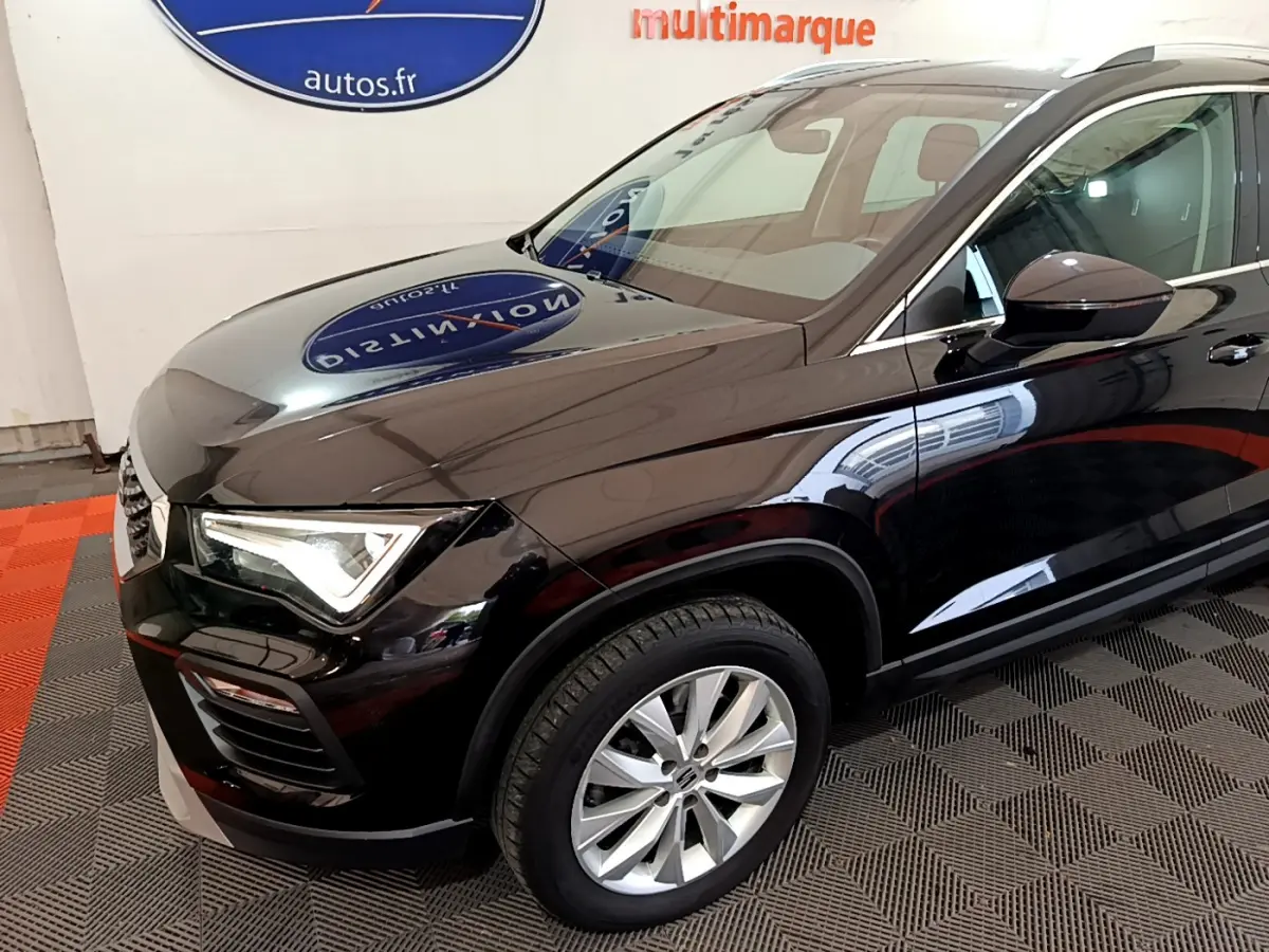 Vue 3/4 avant droit d'un SEAT Ateca noir brillant avec jantes alliage et phares LED allumés en intérieur showroom.