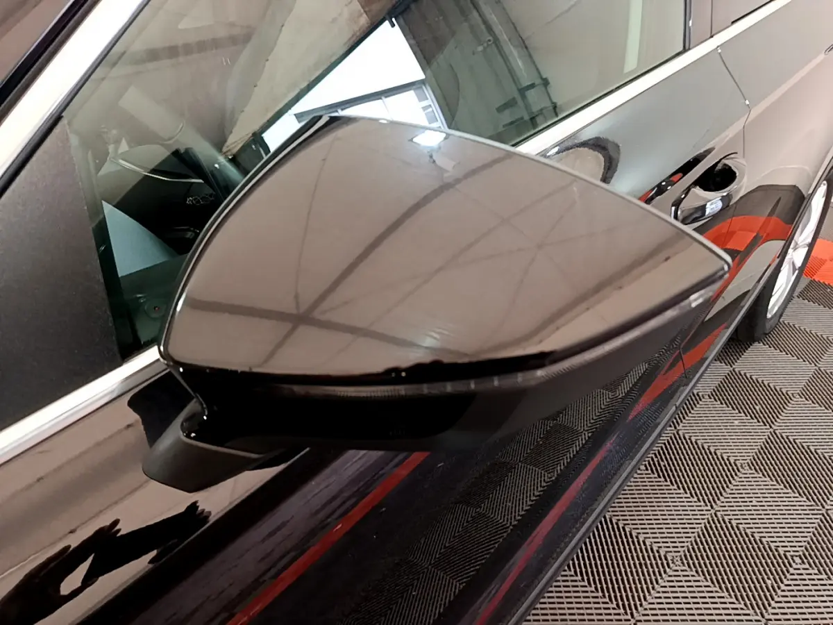 Gros plan sur le rétroviseur côté gauche noir brillant du SEAT Ateca 2022 avec reflet du plafond et carrosserie noire.