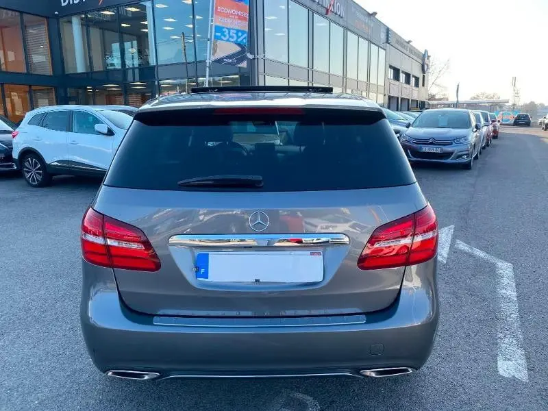 Vue arrière d'une Mercedes Classe B 180 d gris foncé métallisé, avec feux rouges et double sortie d'échappement visible.