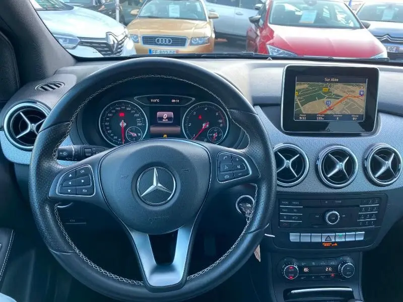 Vue intérieure centrée sur le volant Mercedes Classe B 180 d 2016 avec tableau de bord et écran GPS intégrés.
