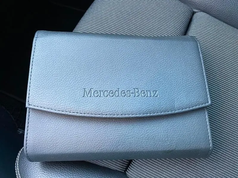 Pochette grise Mercedes-Benz en cuir posée sur le siège avant en tissu gris à motifs blancs du Mercedes Classe B 180 d 2016.