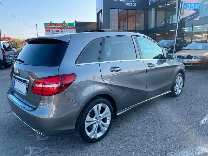 Vue 3/4 arrière droite d'une Mercedes Classe B 180 d gris foncé métallisé, avec jantes alliage et vitres teintées.