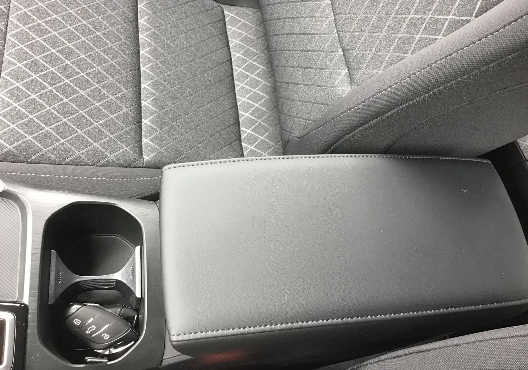 Gros plan sur l'accoudoir central noir et porte-gobelets avec clé de la MG ZS 1.5 L Hybrid+ 2026, sièges tissu gris.